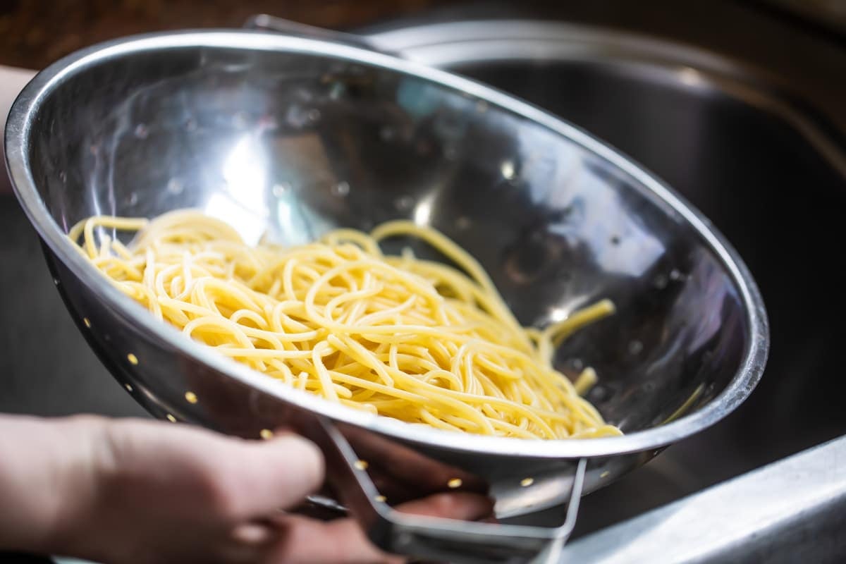 A colander full of cooked spaghetti noodles.