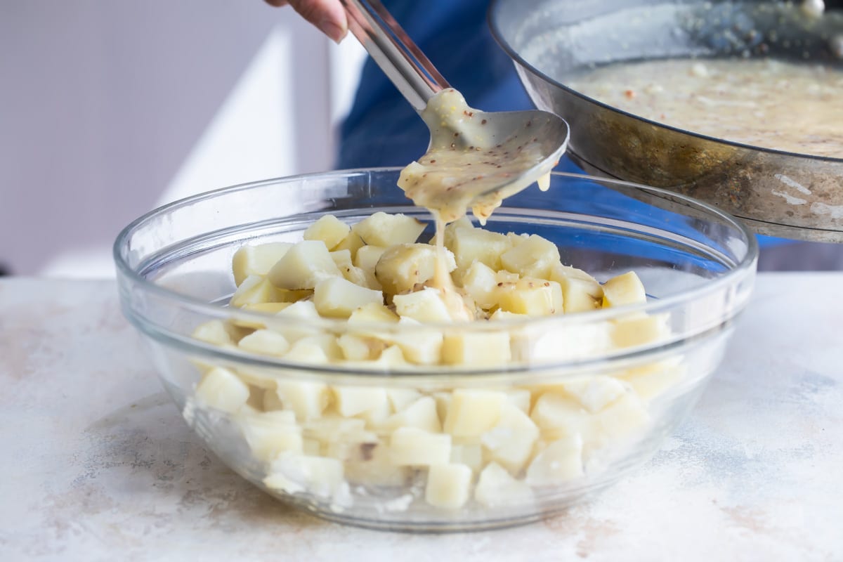 Adding bacon fat to a bowl of potatoes for German potato salad.