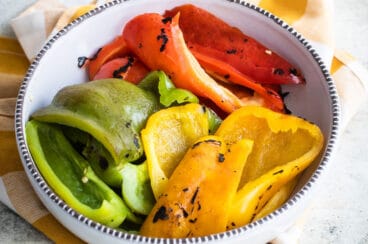 Red, green, and yellow roasted peppers in a bowl.