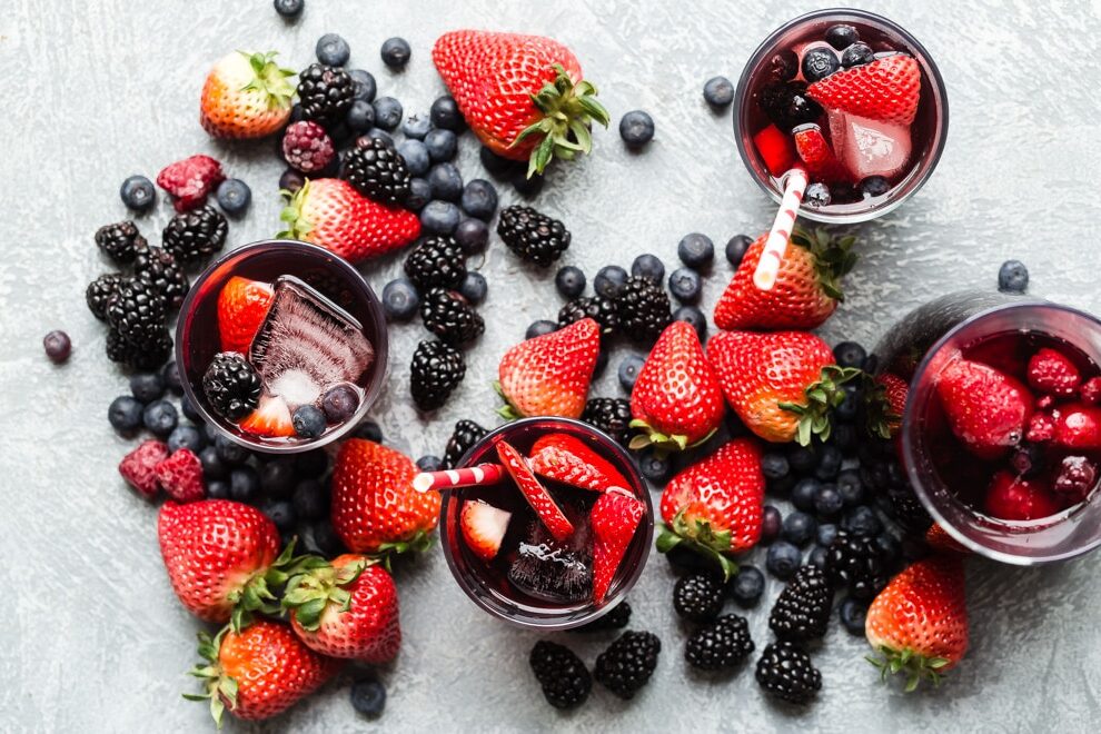 3 glasses and a pitcher of iced tea berry sangria surrounded by piles of fresh berries.
