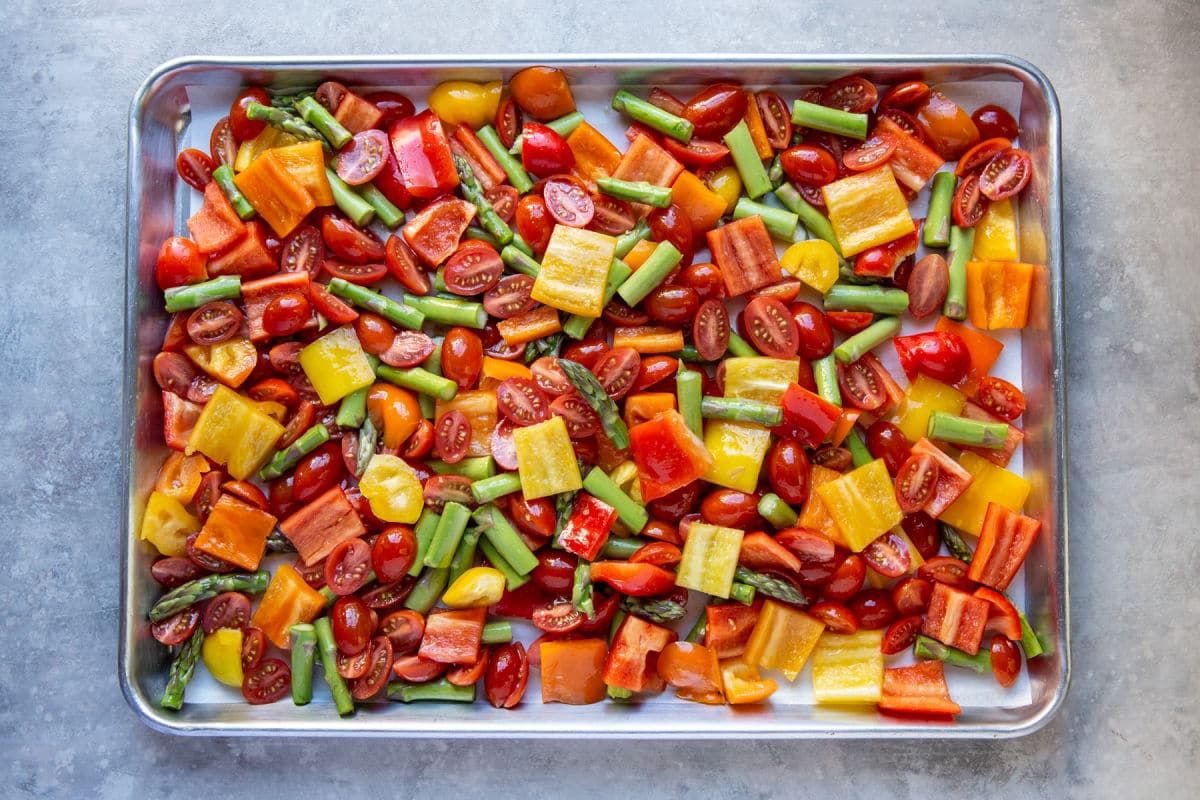 A sheet pan full of chopped peppers, tomatoes, and asparagus ready to be roasted.