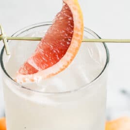A collins glass with a Paloma cocktail in it, garnished with a grapefruit wedge.