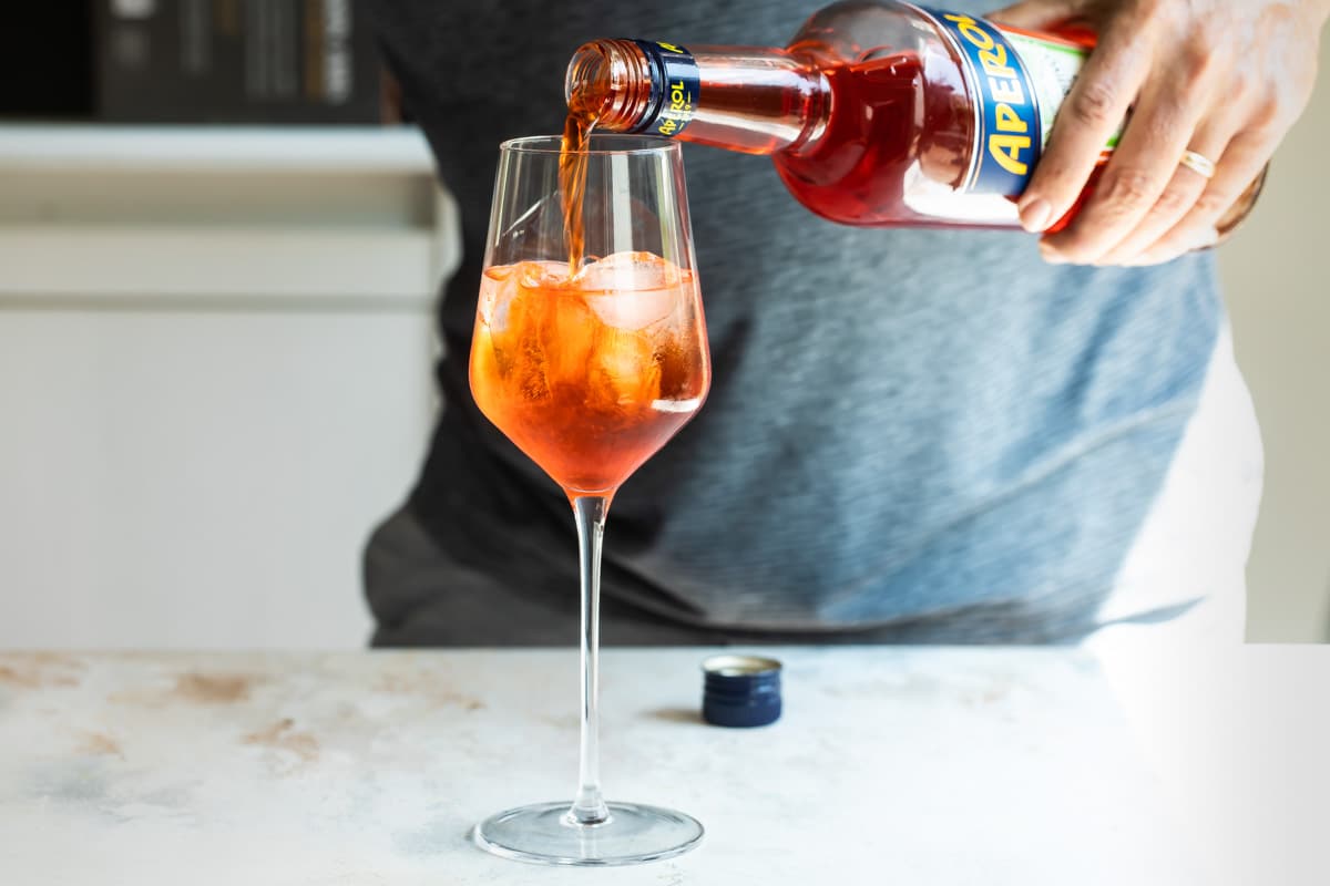 Someone pouring aperol into a glass to make an aperol spritz.