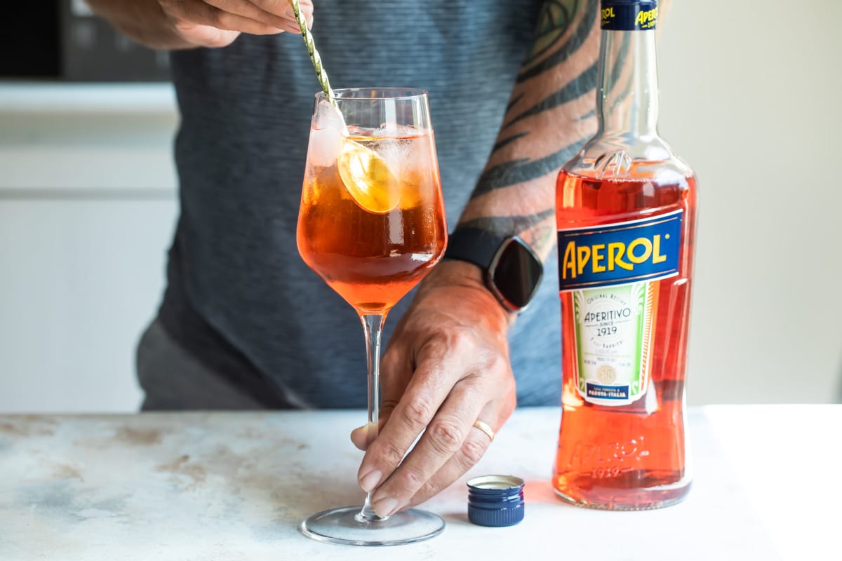 Someone stirring in a glass to make an aperol spritz.