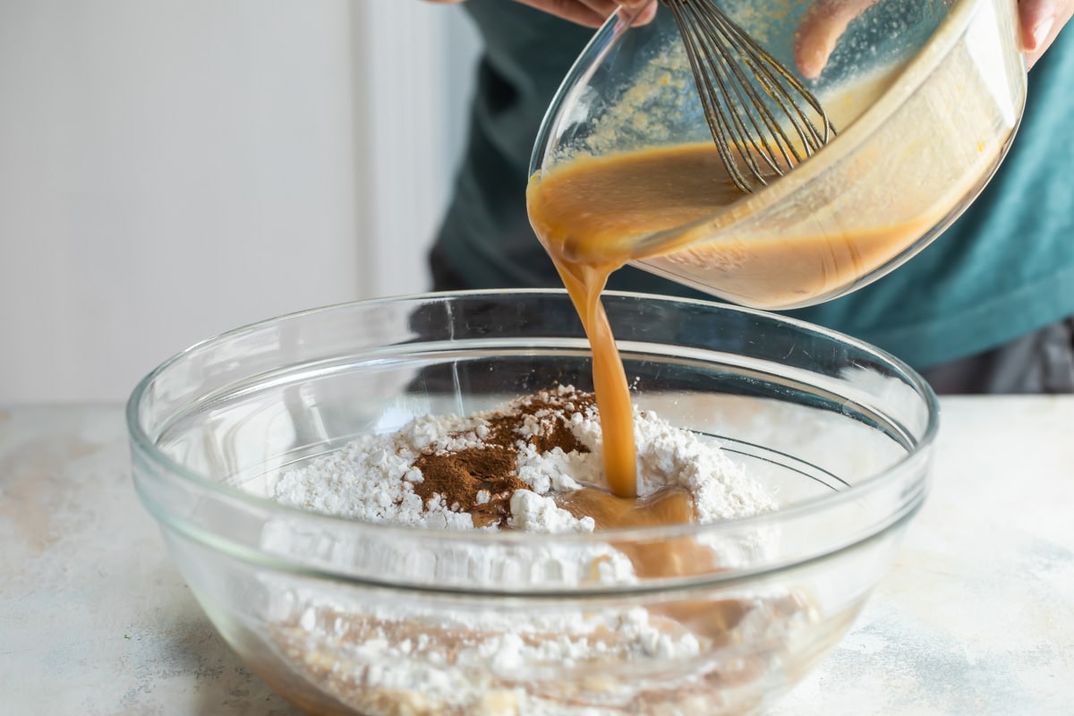 A brown liquid being poured into a clear bowl with flour and other dry ingredients.