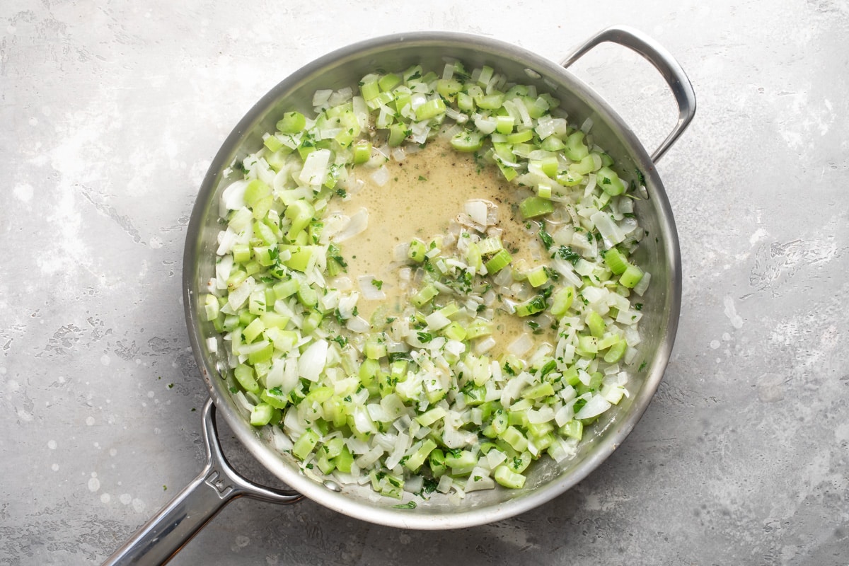 Celery, onions, butter and spices being cooked in a silver skillet.