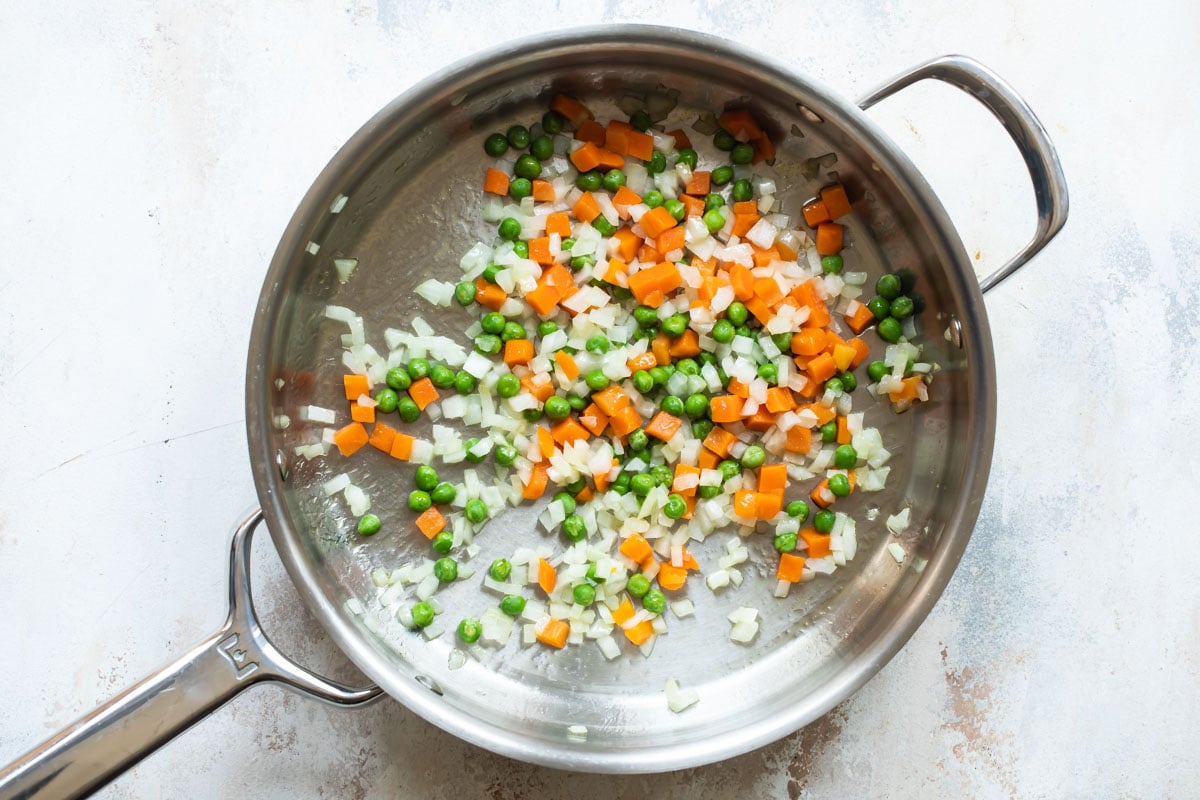 Peas, carrots and onion in a silver skillet.