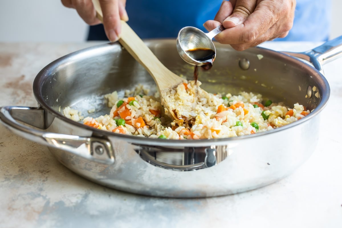 Someone pouring soy sauce into a skillet with brown fried rice.