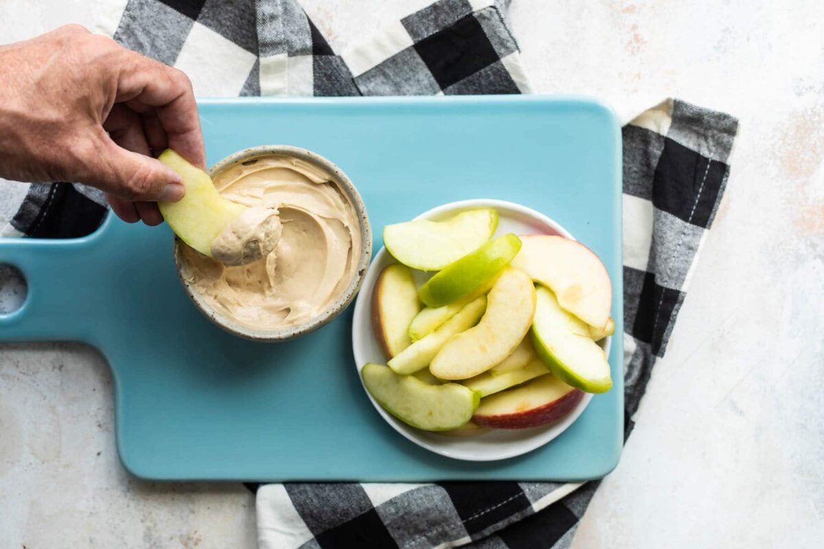 Someone dipping an apple slice into caramel apple dip.