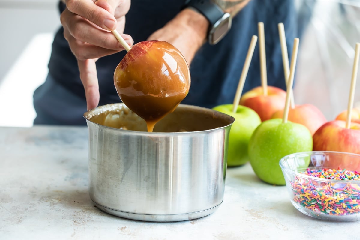 A caramel apple being pulled out of a silver pot after being dipped.