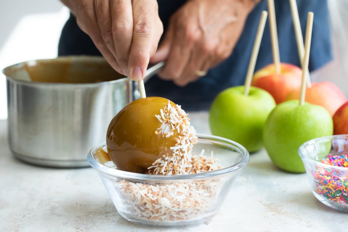 A caramel apple being dipped in toasted coconut.