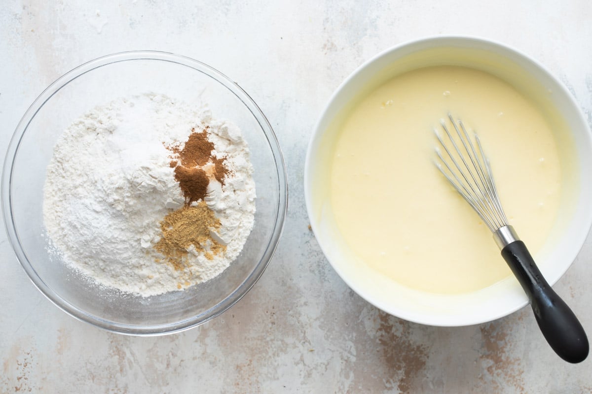 A bowl of dry ingredients next to a bowl of batter with a whisk in it.
