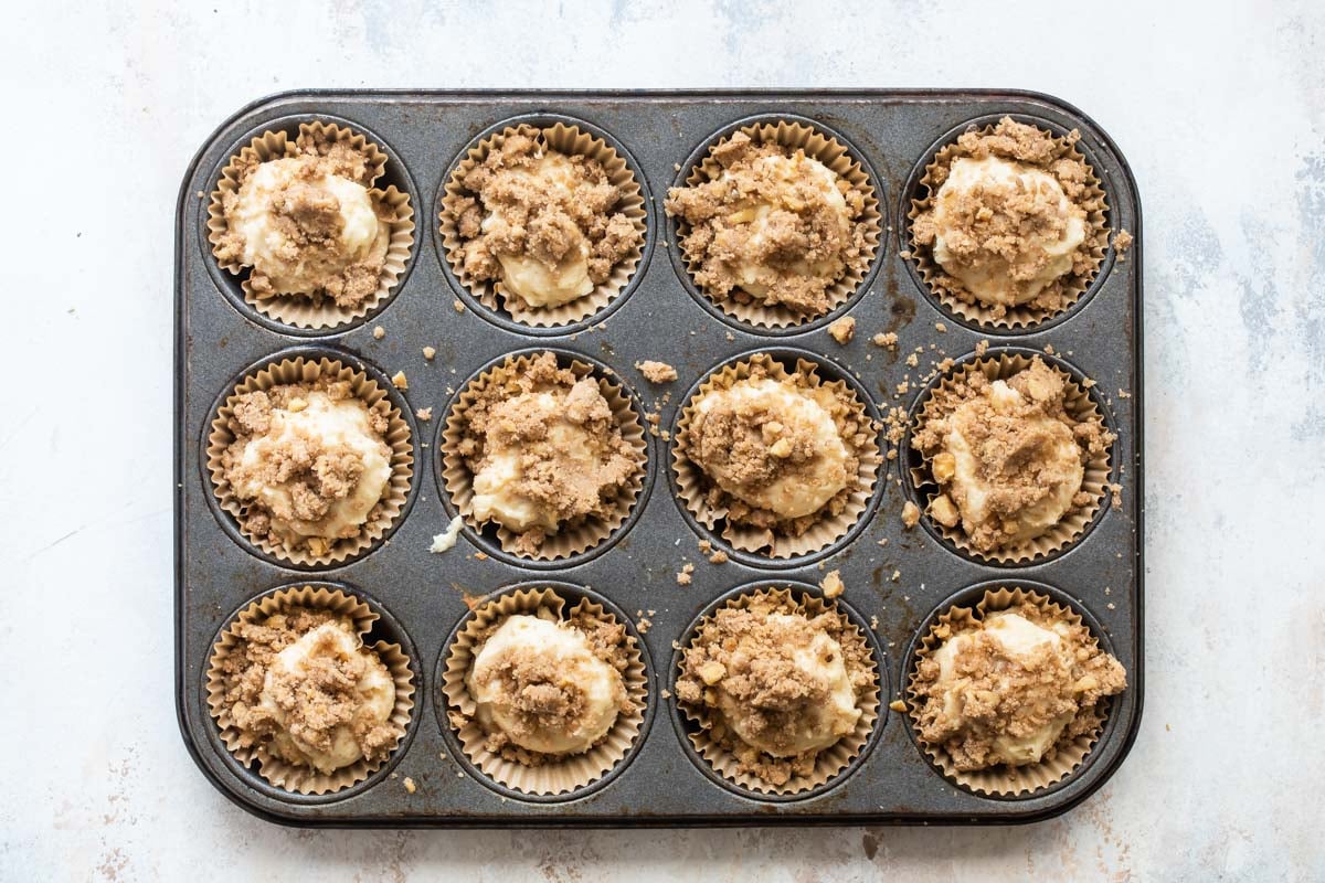 Twelve coffee cake muffins before being baked in a muffin tin.