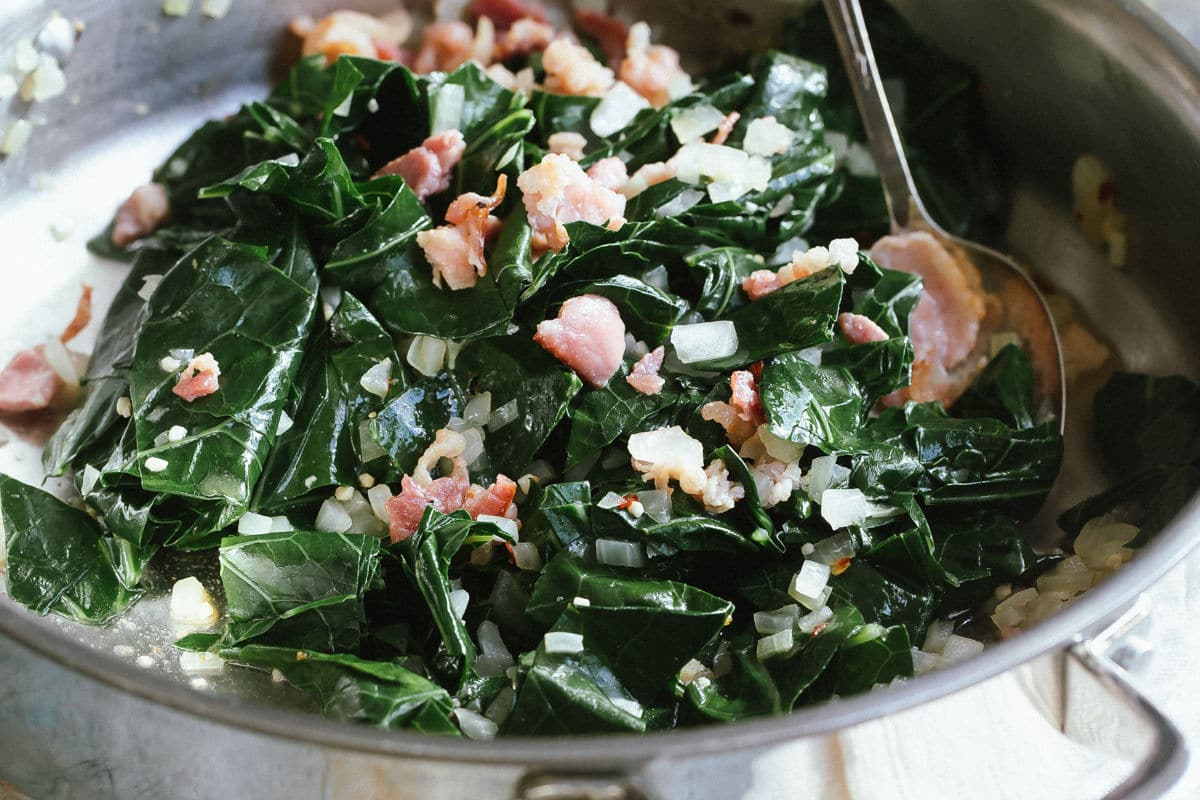 A skillet full of collard greens with bacon.