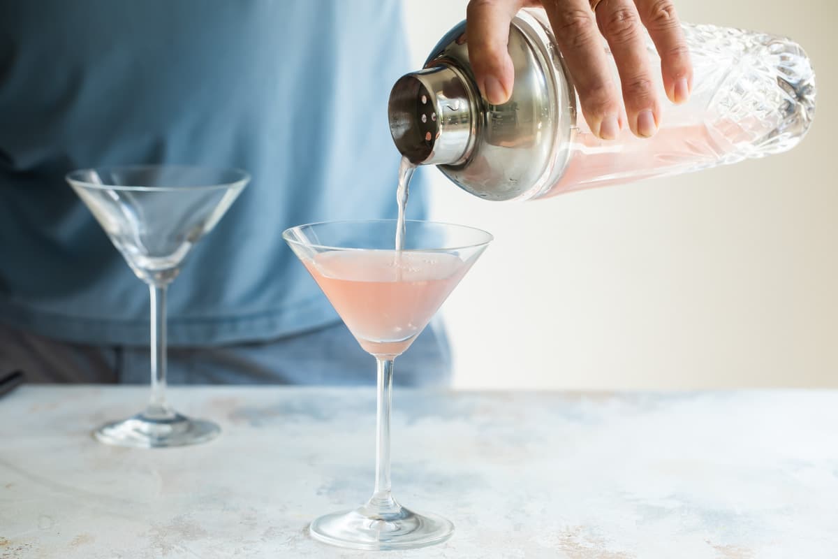 Pouring a cosmopolitan cocktail into a glass.
