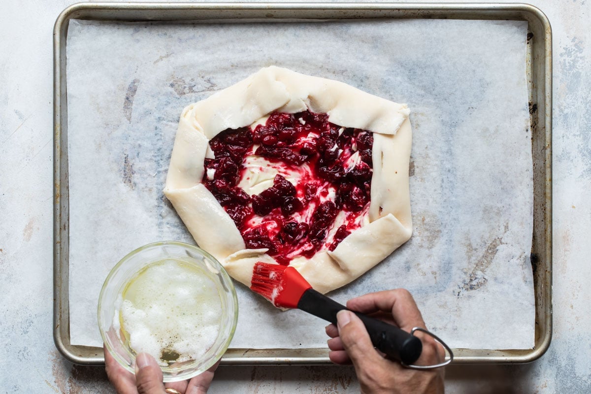 An uncooked cranberry cheesecake galette on a piece of parchment paper on a baking sheet.