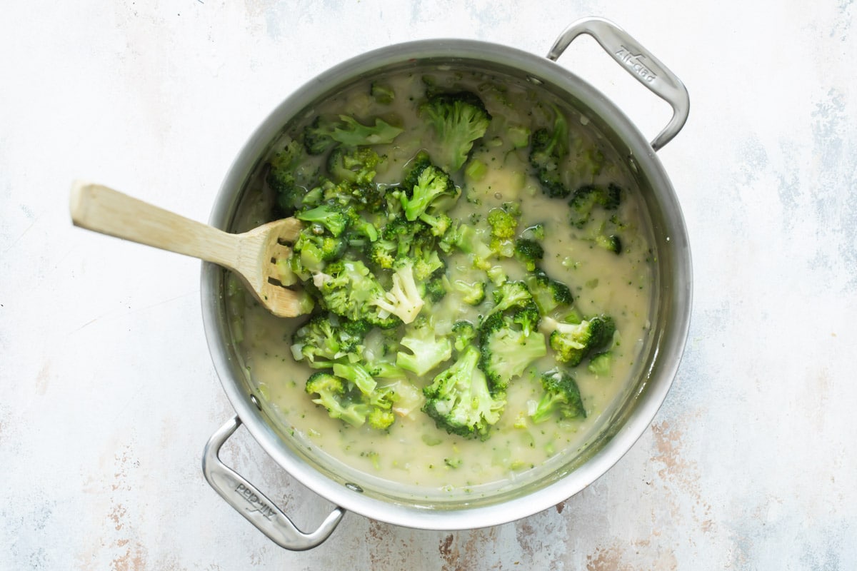 Broccoli being cooked in a silver stockpot with a yellow liquid.