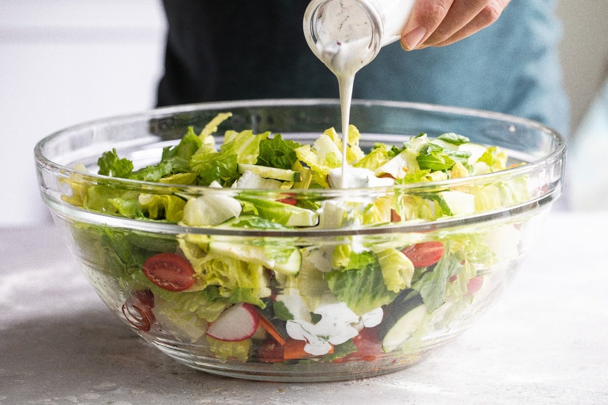 Ranch dressing being poured onto an easy garden salad in a clear bowl.
