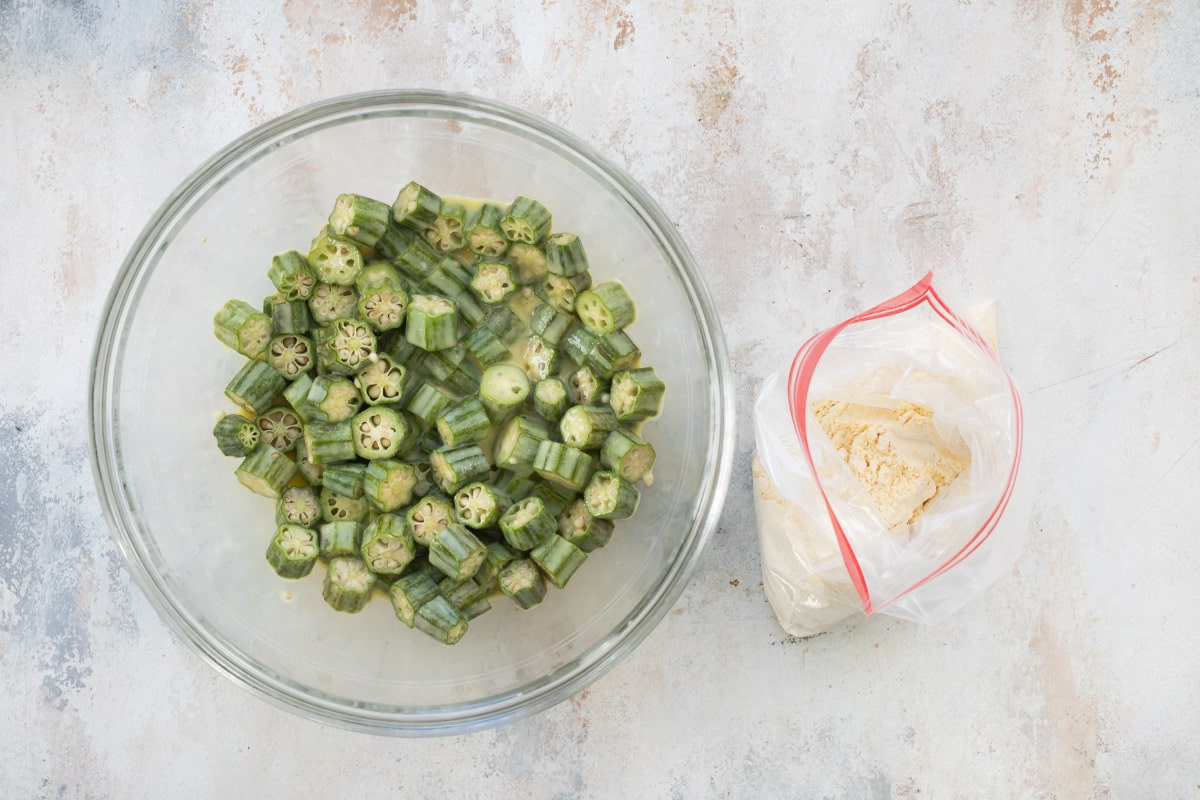 Okra soaking in buttermilk next to a bag of crumb coating.