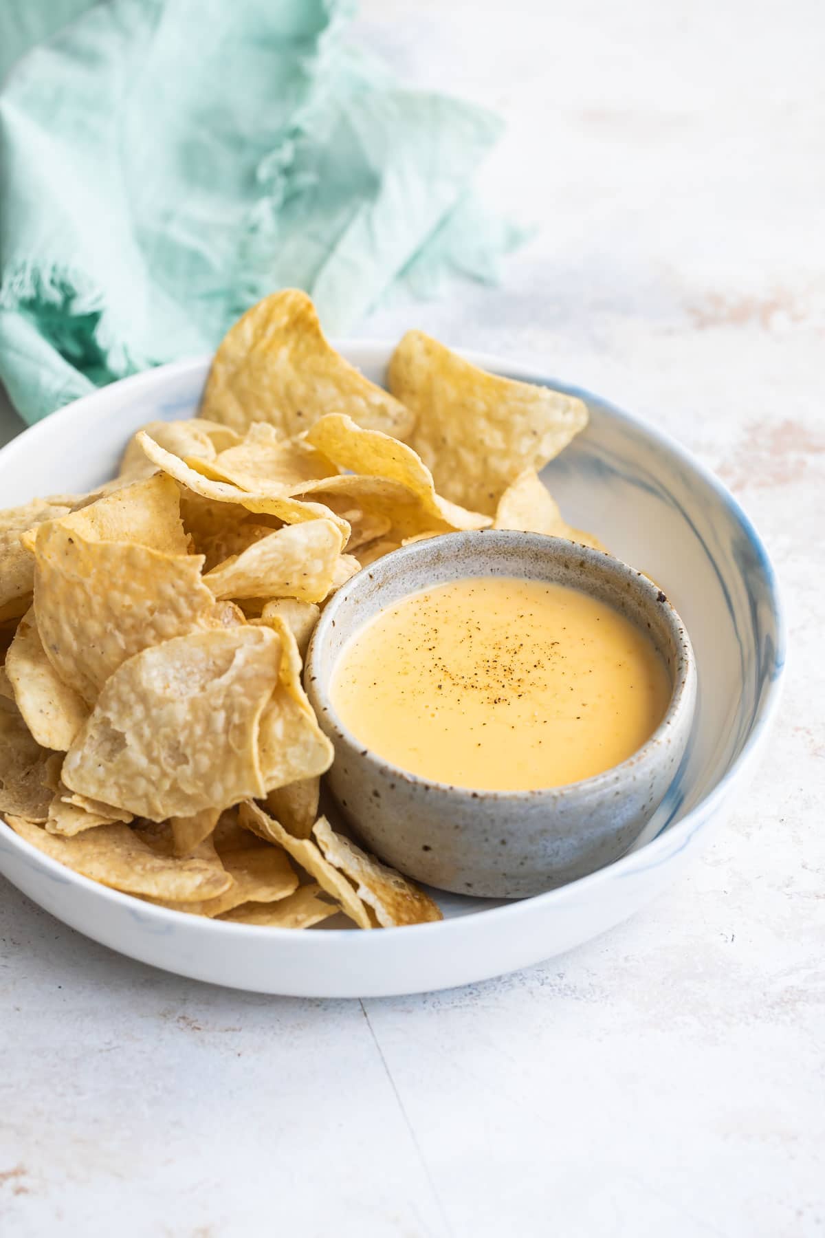A bowl of cheese sauce with tortilla chips on a platter.
