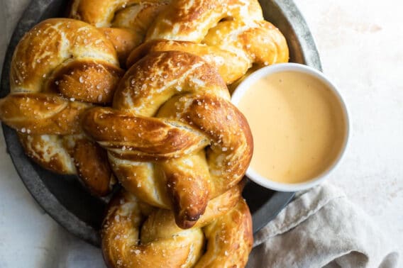 A platter of soft pretzels with a bowl of cheese sauce.