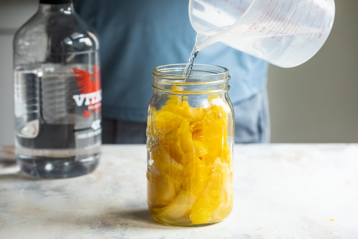 Someone pouring clear liquid into a jar with lemon segments.