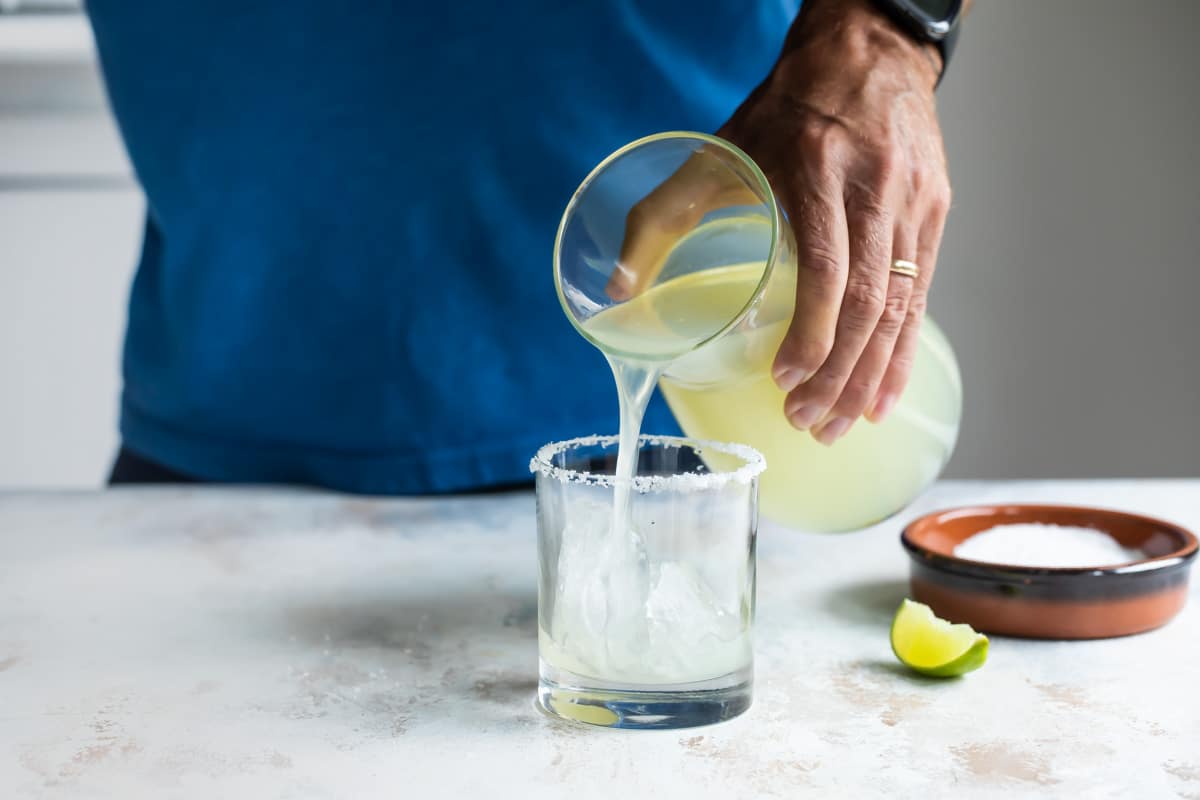 Someone pouring a margarita in a glass.