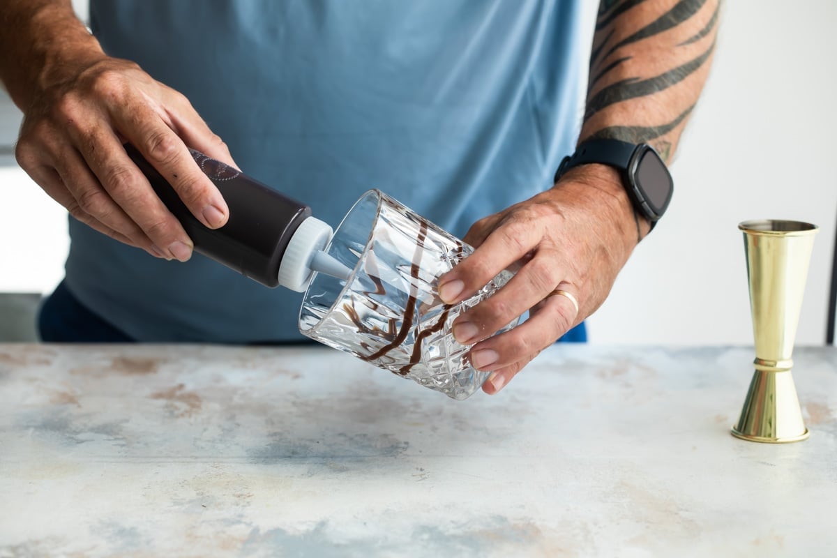 Adding chocolate syrup to a glass for a mudslide.