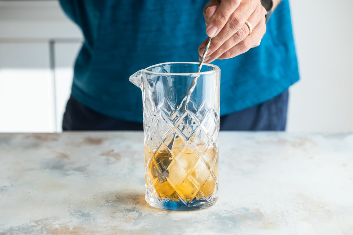 Mixing an Old Fashioned cocktail in a glass mixing glass.