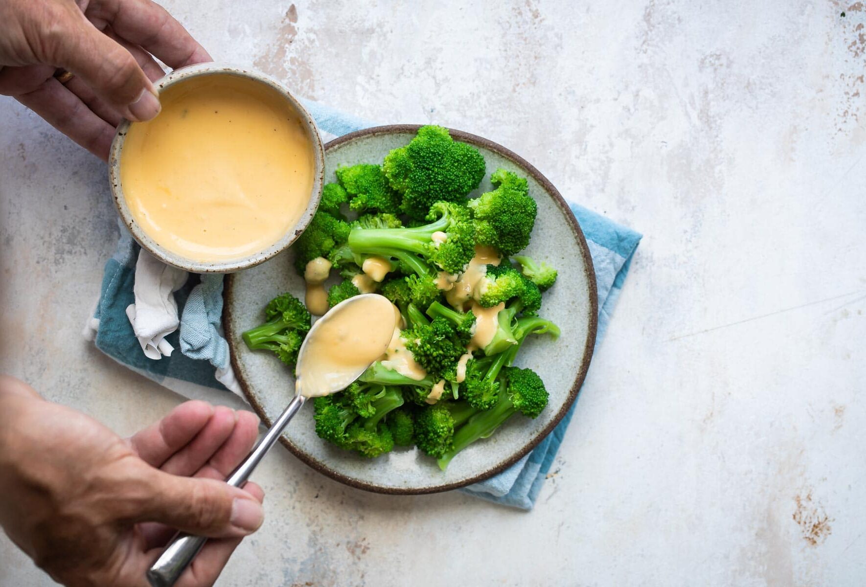 Blanched broccoli on a plate with cheese sauce.
