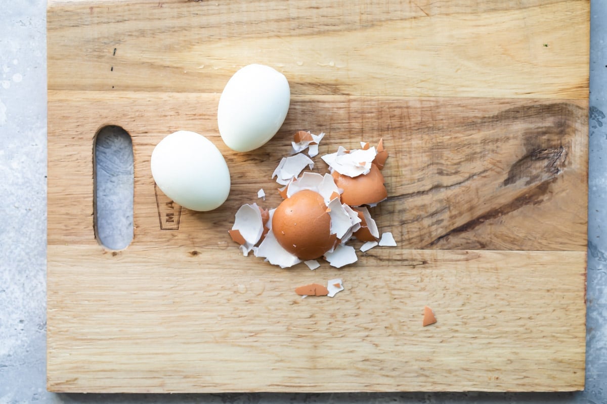Peeling hard boiled eggs on a cutting board.