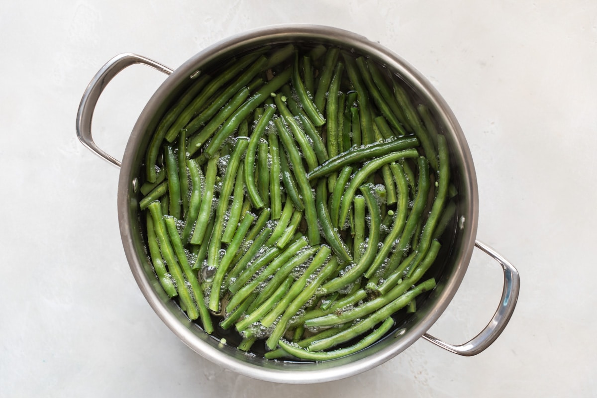 Green beans being boiled in water in a silver pot.