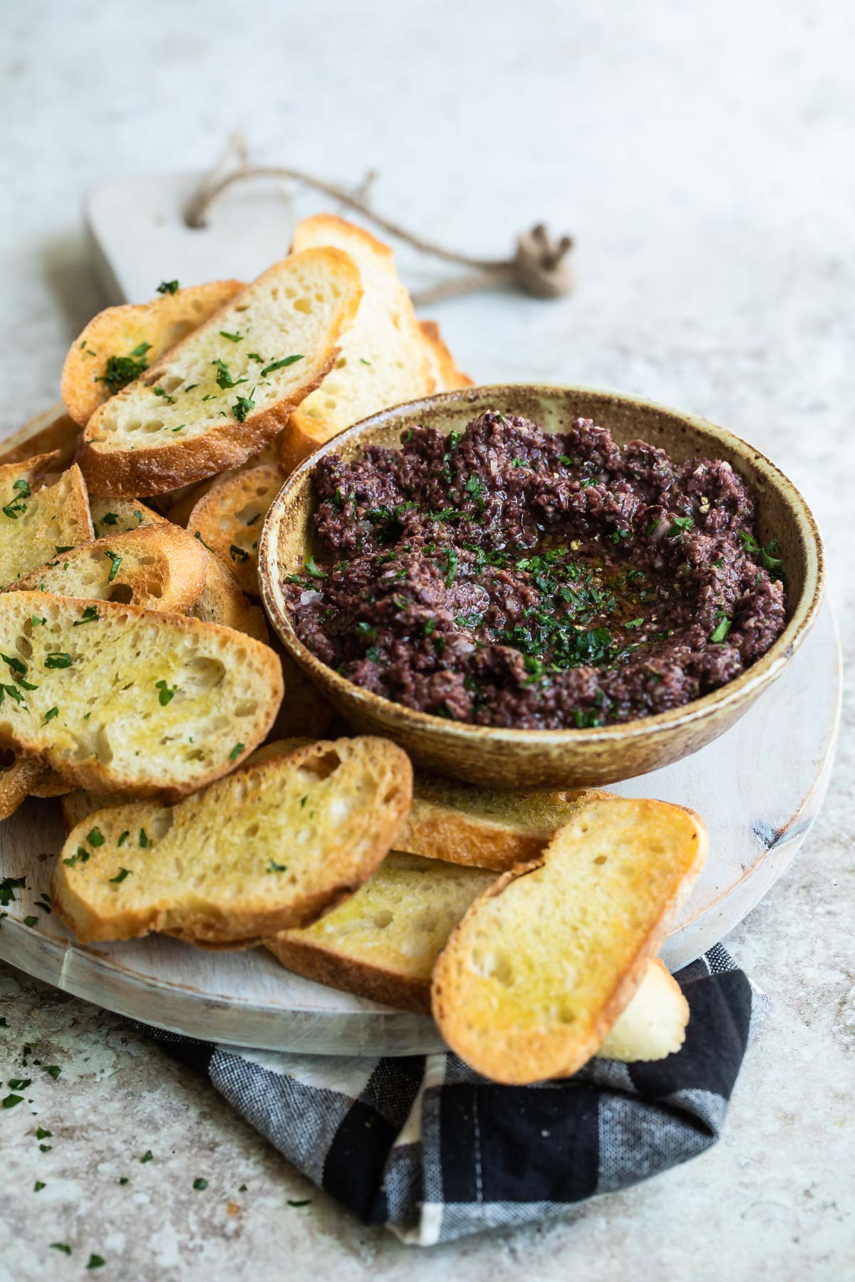 Homemade olive tapenade in a bowl surrounded by toasted bread.