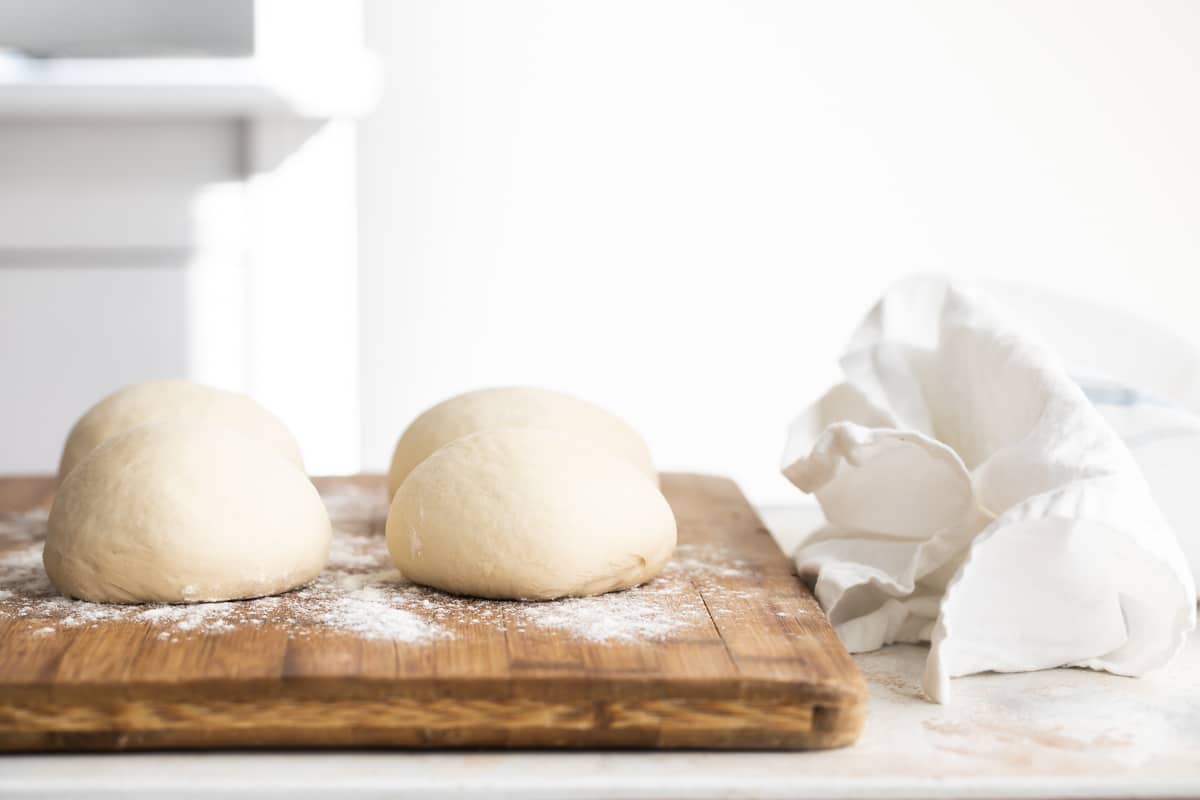 Four balls of homemade pita bread dough on a cutting board.