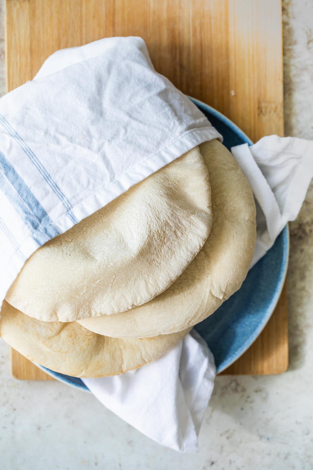 Homemade pita bread wrapped in a white towel on a plate.