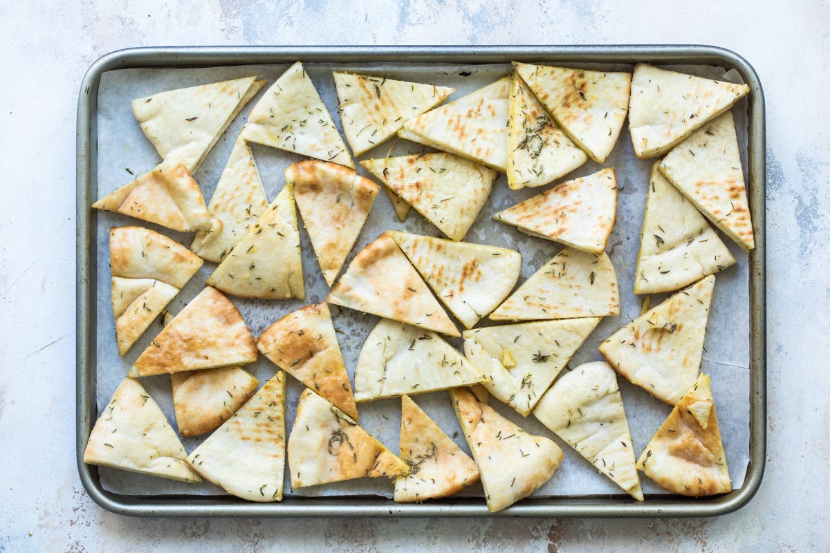 Seasoned triangle slices of pita bread on a baking sheet.