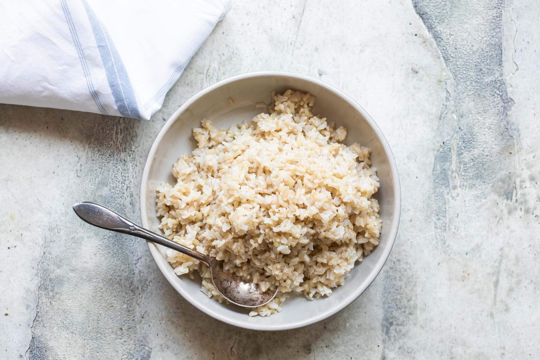 A bowl of brown rice with a silver spoon resting in it.