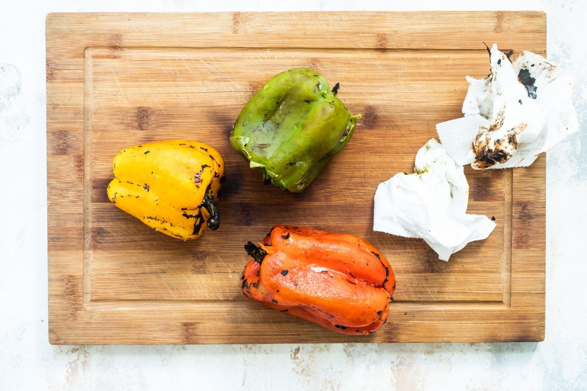 Roasted red, green, and yellow pepper on a wood cutting board.