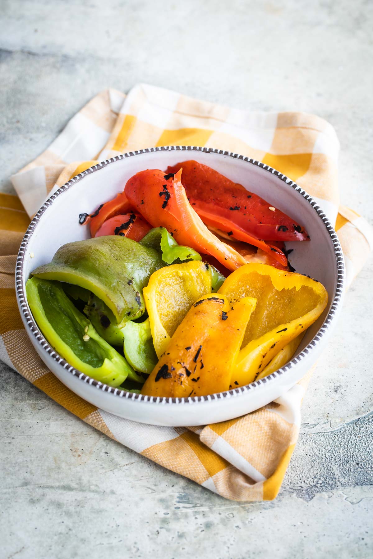 Red, green, and yellow roasted peppers in a bowl.