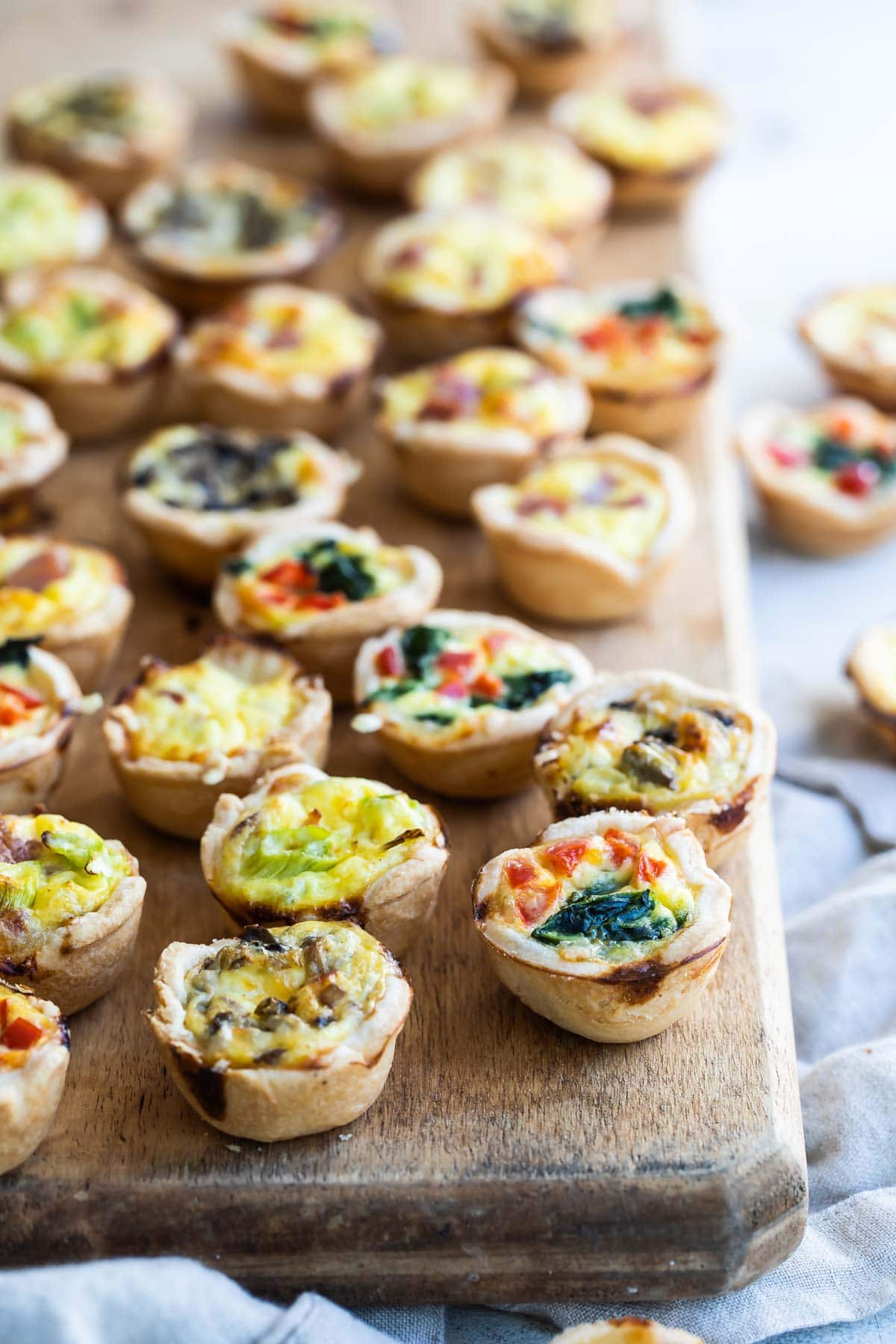 A wooden board filled with 4 varieties of mini quiche.