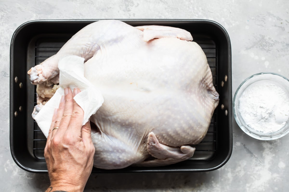 Patting a raw turkey dry with paper towels.