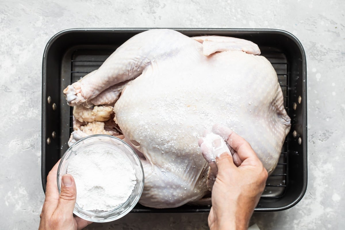 Patting a dry brine on a raw turkey.