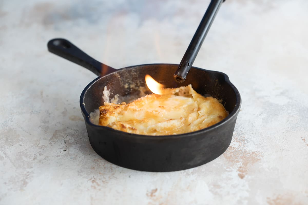 Saganaki in a small cast iron pan being heated with a lighter.