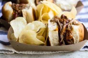 A paper food boat with a pulled pork sandwich and potato chips.
