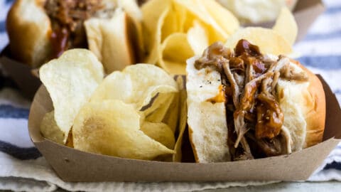 A paper food boat with a pulled pork sandwich and potato chips.