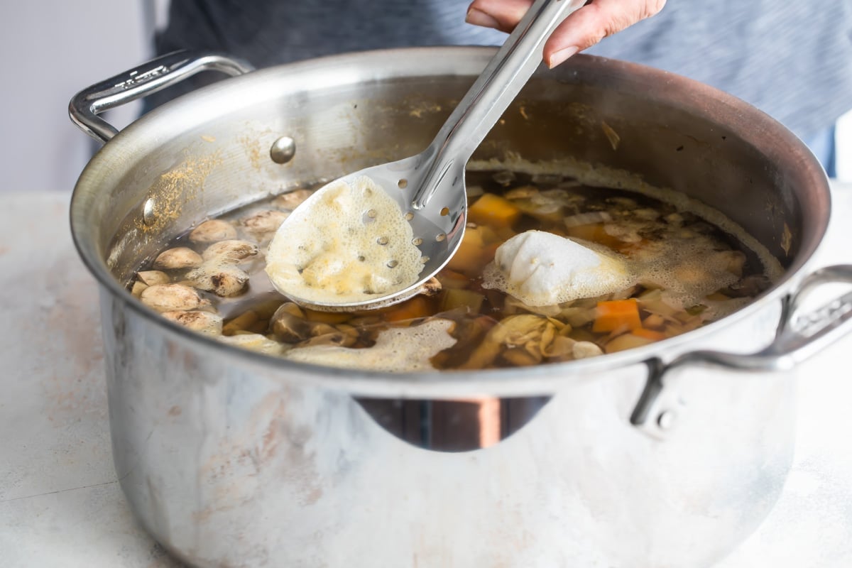 Someone stirring boiling vegetables and their stock in a silver pot with a slotted spoon.