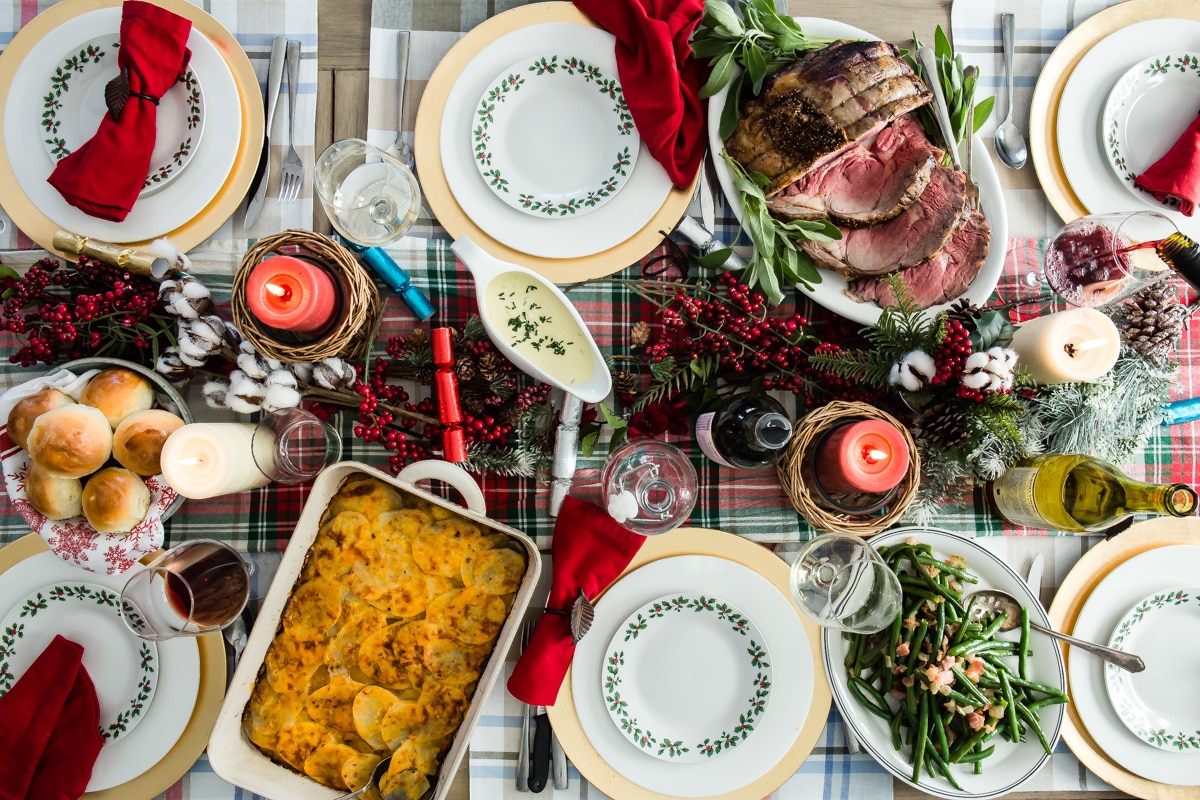 A Christmas table with prime rib, scalloped potatoes, green beans, and rolls.