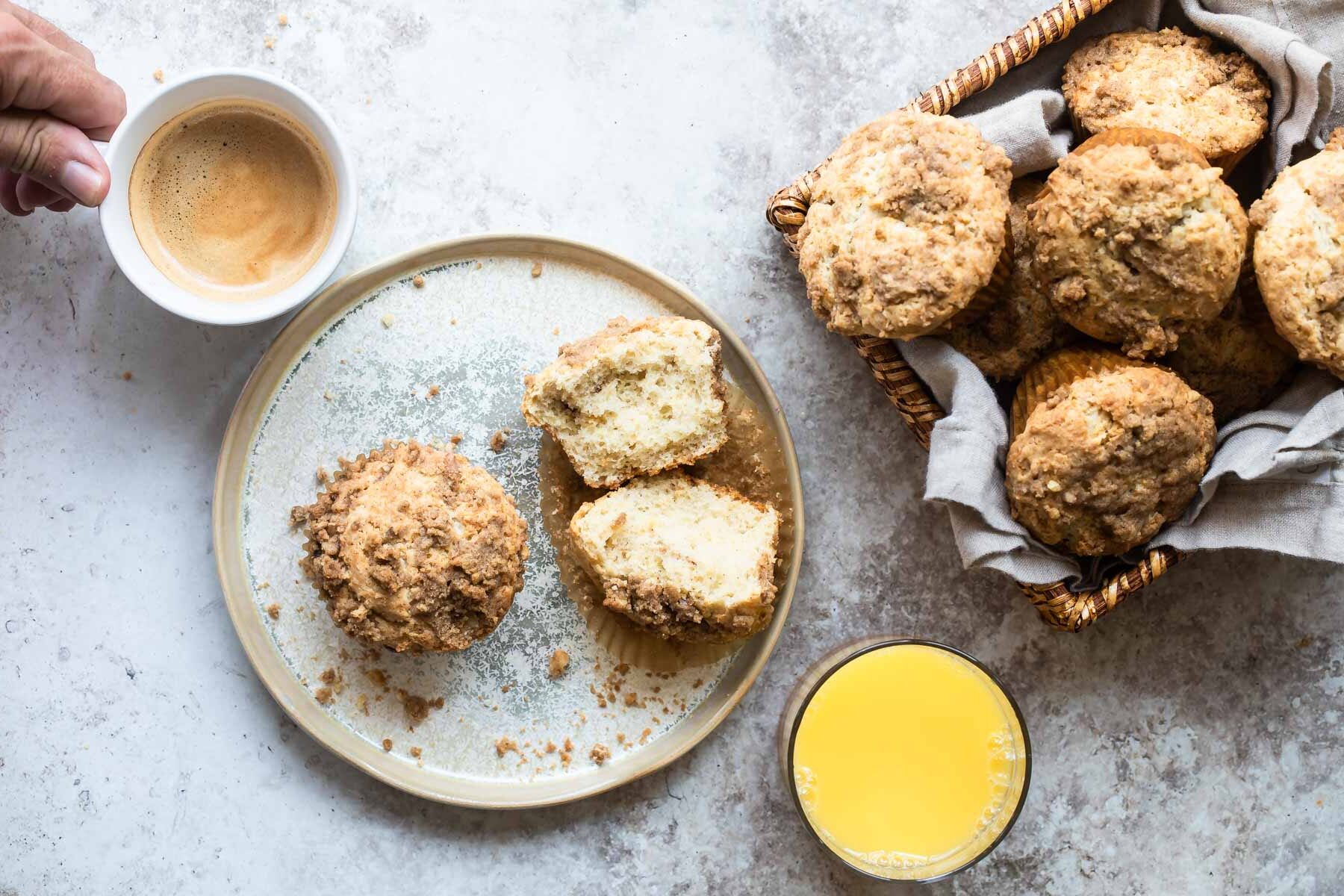 Two coffee cake muffins on a plate next to a cup of coffee and a cup of orange juice.