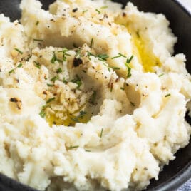 Garlic mashed potatoes in a black bowl with a serving spoon on a blue and white striped towel.