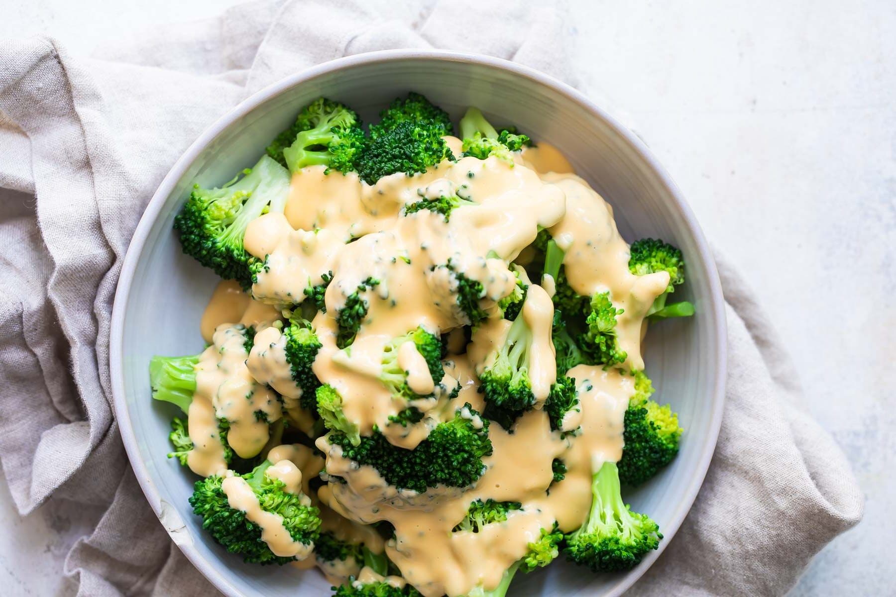 A bowl of blanched broccoli with cheese sauce drizzled on top.